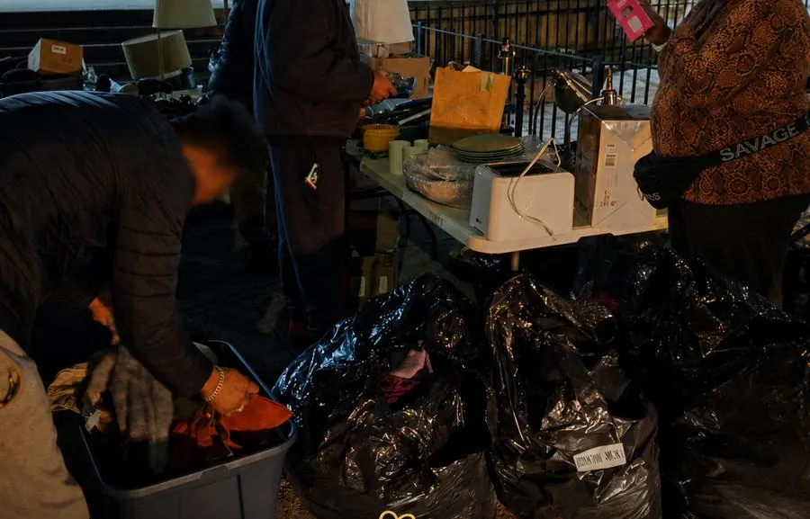 Residents browsing tables of lamps, dishes, and a toaster at night outside a NYCHA building