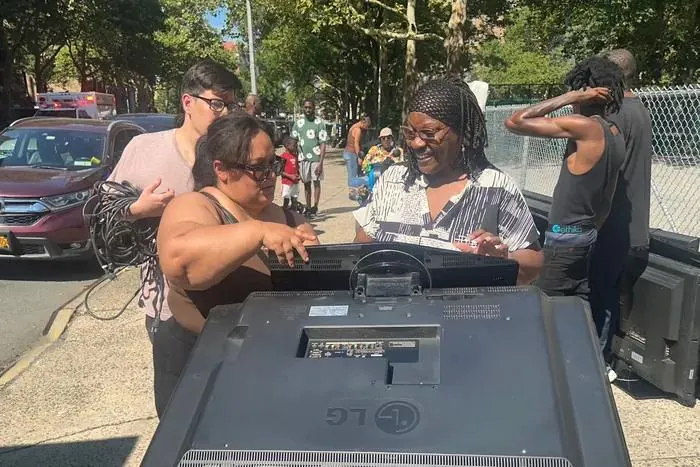 Two women laughing as they look over a donated flat-screen TV on the sidewalk